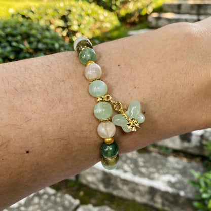 Bracelet with green and pink beads and a gold charm on a wrist outdoors.