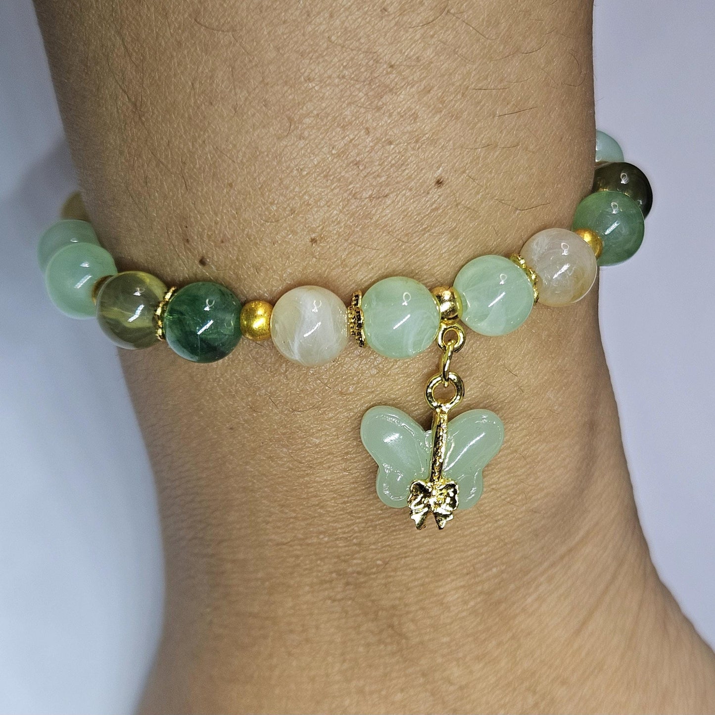 Green beaded bracelet with a butterfly charm on a wrist against a white background