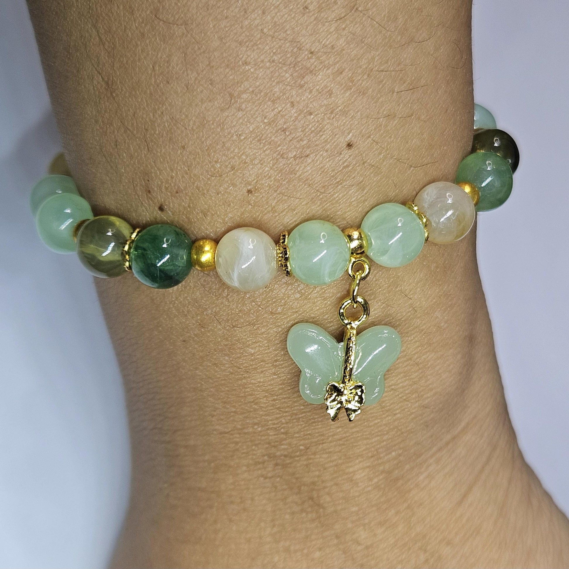 Green beaded bracelet with a butterfly charm on a wrist against a white background