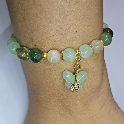 Green beaded bracelet with a butterfly charm on a wrist against a white background